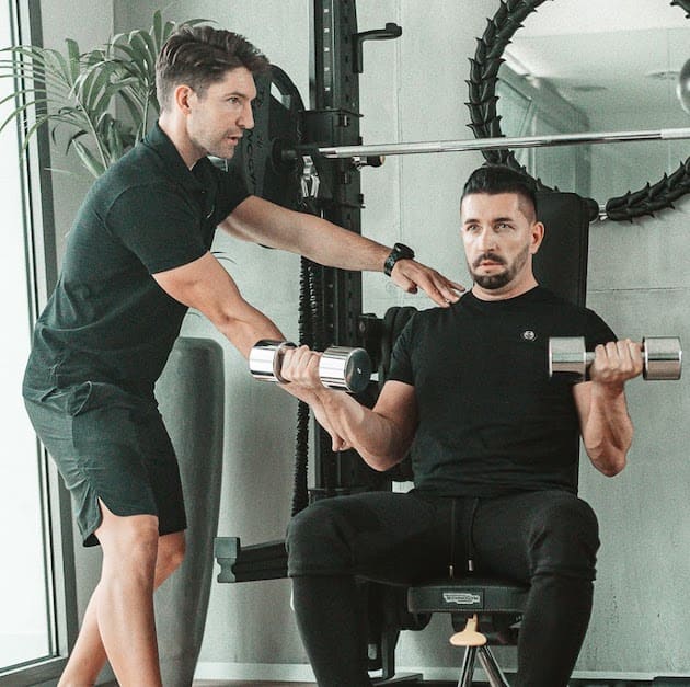 A Reset Studio trainer coaching a man through a dumbbell press